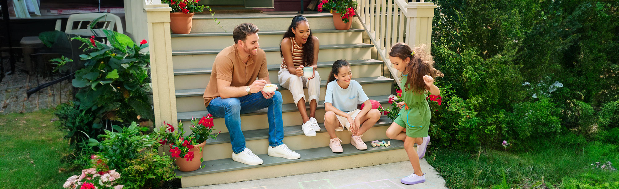 Family sitting on front steps enjoying breakfast while kids play